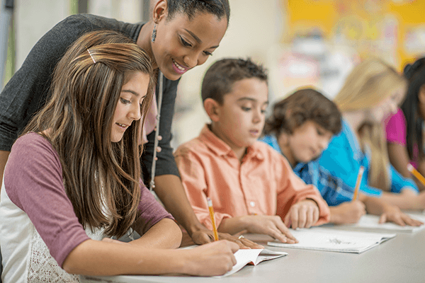 A photograph of a teacher working with students on a writing project in a classroom.