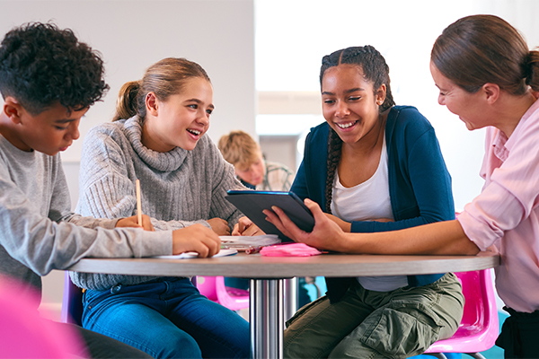 A teacher is teaching media literacy to students by showing them how to compare different websites on a tablet.
