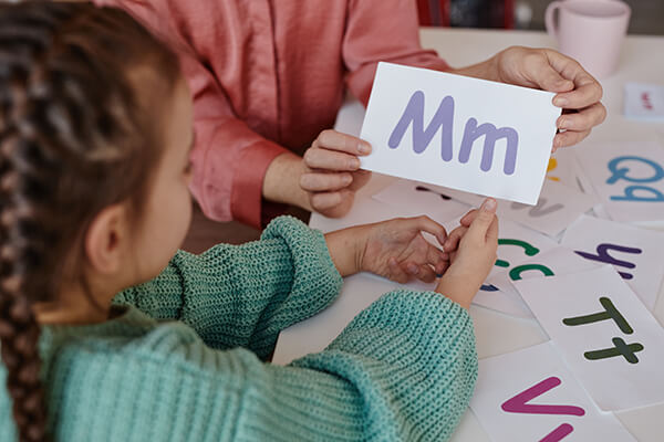 Photo of a teacher showing an alphabet card with an uppercase M and lowercase m to a student during a lesson about print concepts.