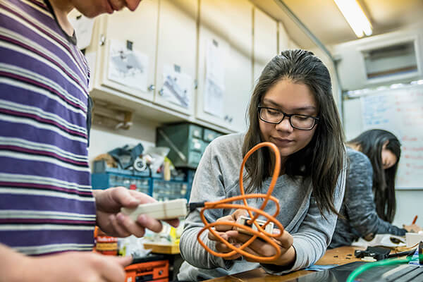 Two students are conducting a science experiment in a classroom using electrical cords.