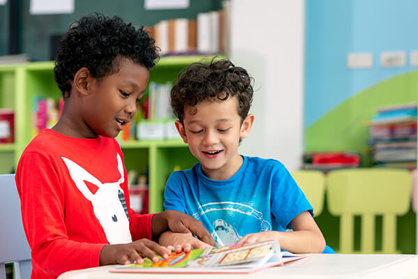 Two young students having an active conversation about a book they are reading in a classroom.
