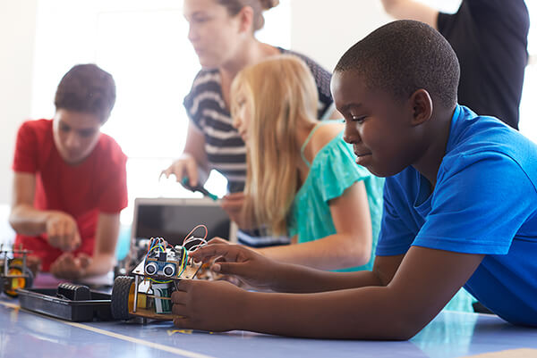 A student leans over a table building a robot in STEM class.