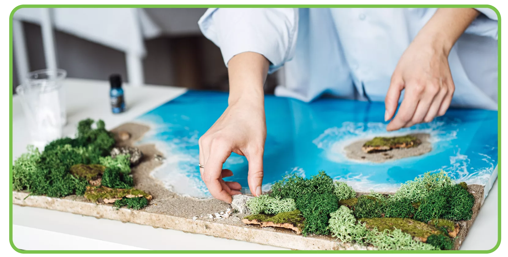 An individual builds a model of a wetland, with water, sand, and small plants, as part of a background-building activity prior to reading complex text.
