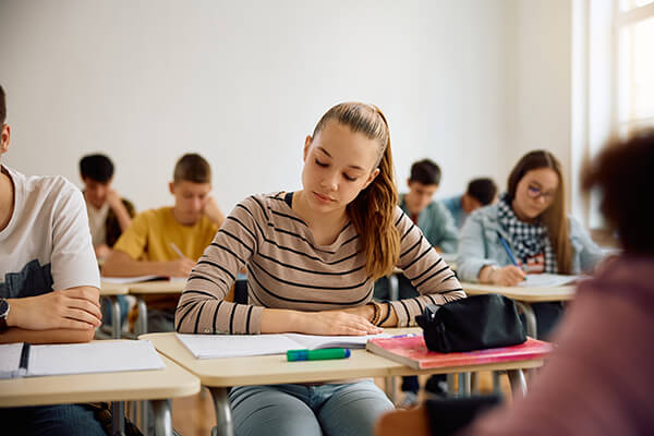 An older female student sits reading at her desk in a classroom.