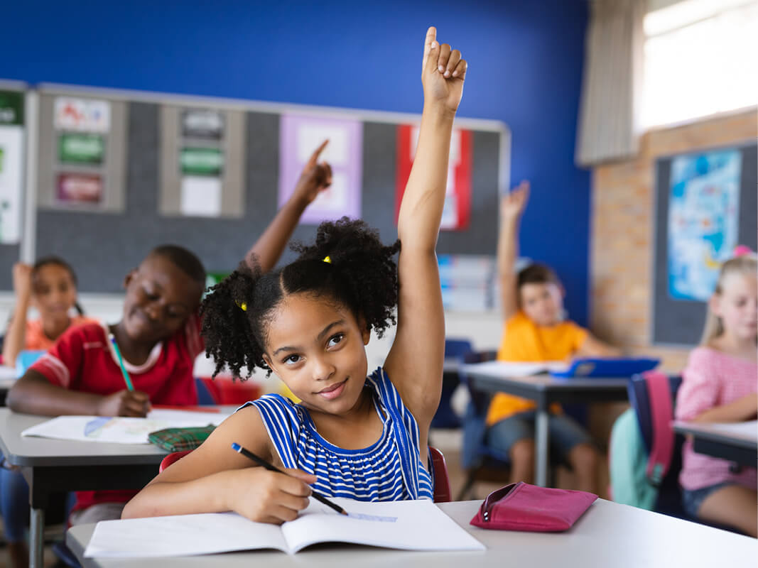 A student in a science classroom raising her hand to ask a question about phenomena.