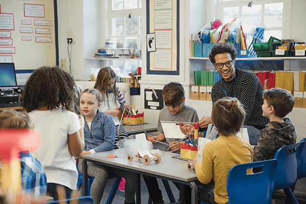 A photograph of a teacher happily working with a small group of young students.