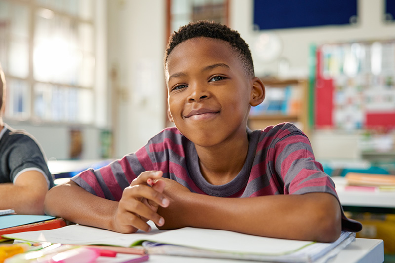 A photo of a happy independent student at a desk in a classroom.