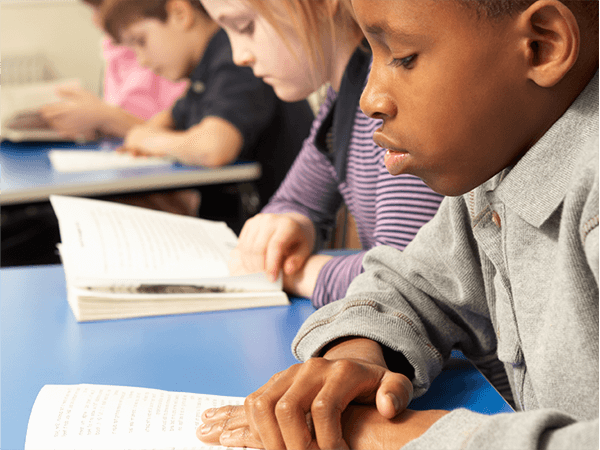 This photo shows a teacher reading an authentic text aloud to a group of students, encouraging the building of background knowledge and vocabulary, discussion and collaboration.