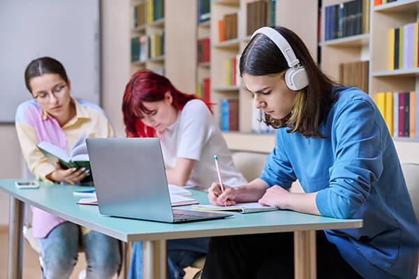 A multilingual high school student in a classroom with headphones on receiving audio support in their home language.