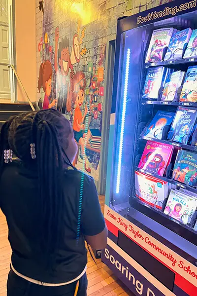 A student at the Susie King Taylor Community School stands at the book vending machine, thoughtfully considering her next read.