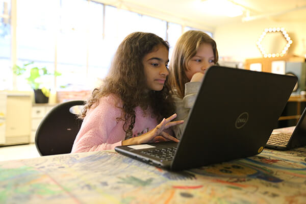 Two Seattle Public Schools students working together in front of a laptop in a classroom.