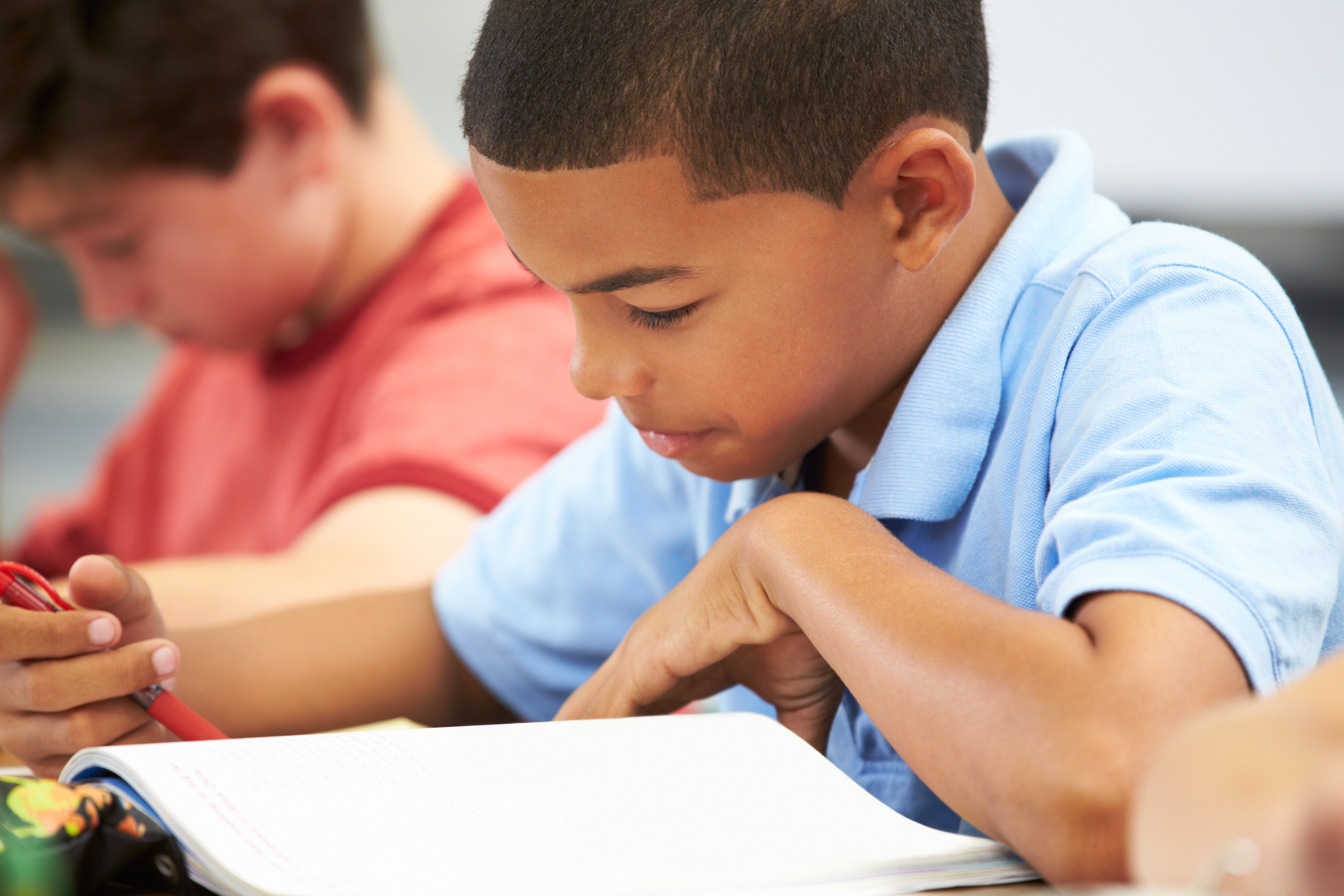 Middle school student concentrating on his work at his desk writing in a notebook.