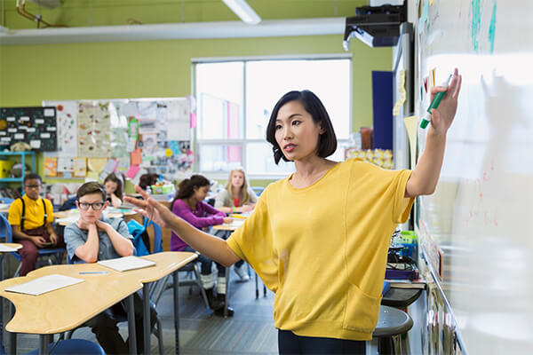 A teacher is standing in front of a whiteboard modeling a concept for the classroom of students.