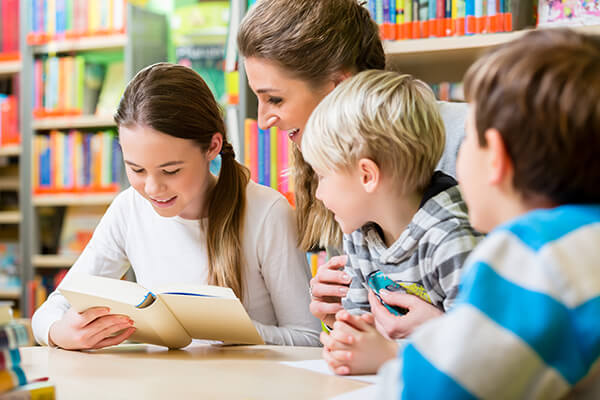 A teacher working with a small group of middle school students on a literacy assignment in a classroom.