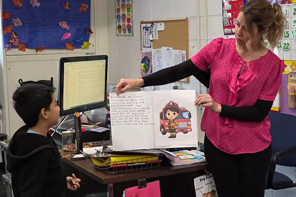An Avondale School Teacher in Auburn Hills, MI holds up a text for a student during a literacy lesson with myView Literacy from Savvas Learning Company.