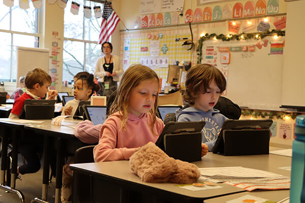 A classroom of students in the Seattle Public Schools district engaging in math discussions while working with tablets at their desks.