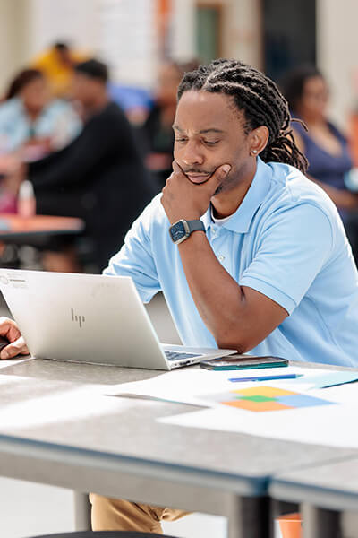 A Clayton County Public Schools teacher sits thinking in front of a laptop at a professional development training.