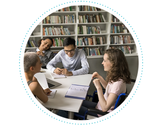 A student in a wheelchair sits at a table completing an assignment with her classmates.