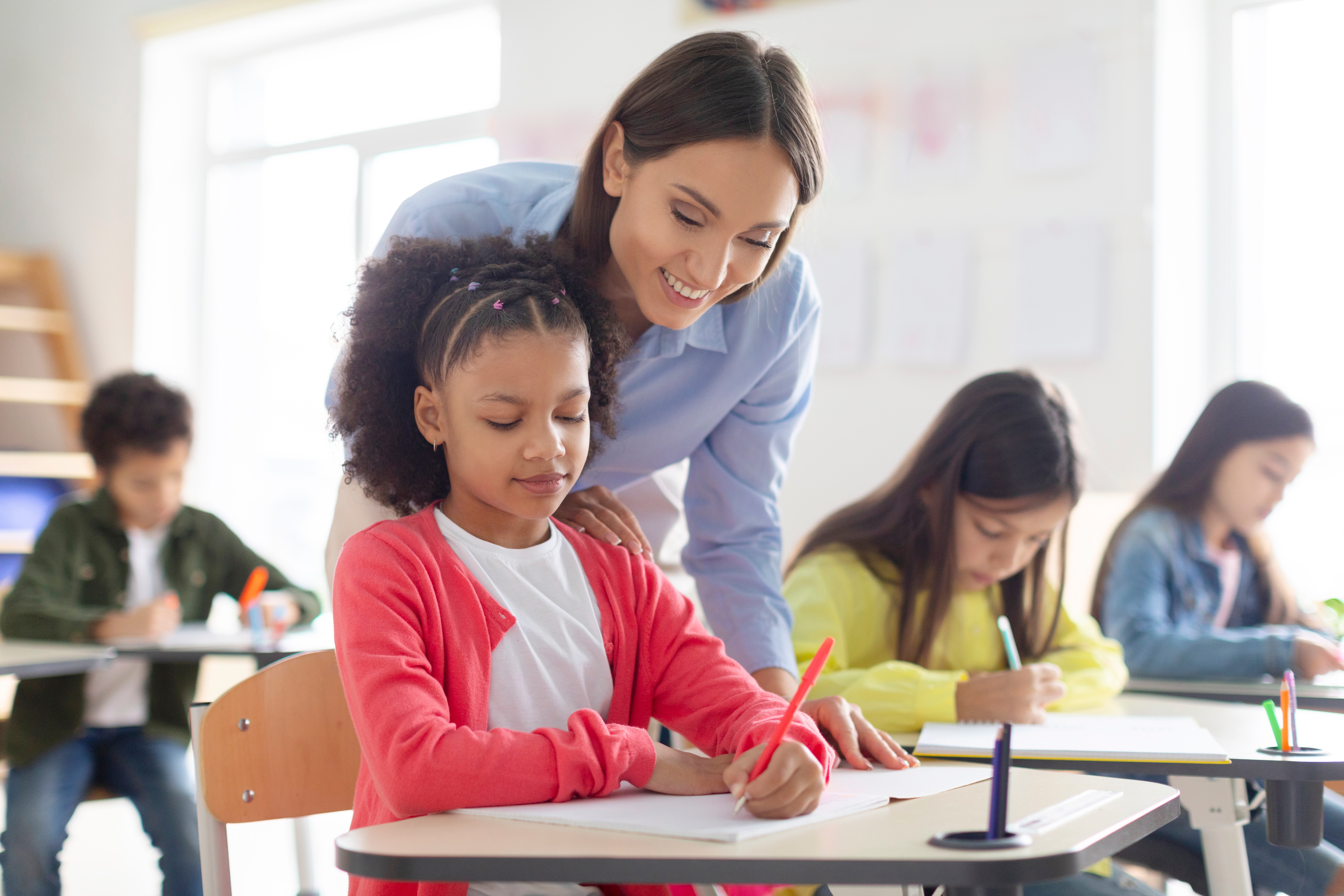 A teacher working with an elementary-aged student on a writing assignment in the classroom..