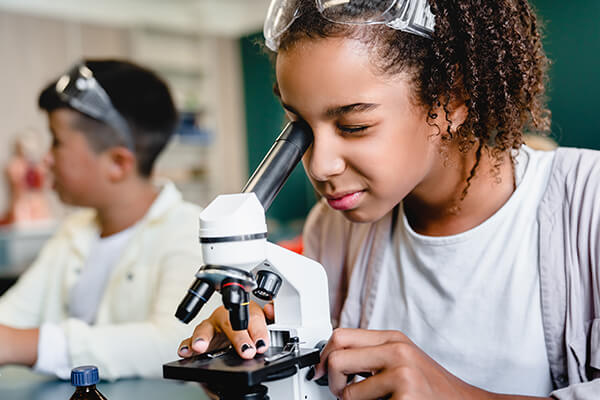 Middle-school-aged girl looking through the lens of a microscope.