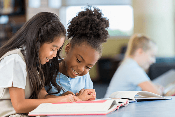 A photograph of two students happily working together at their desks on a writing project.
