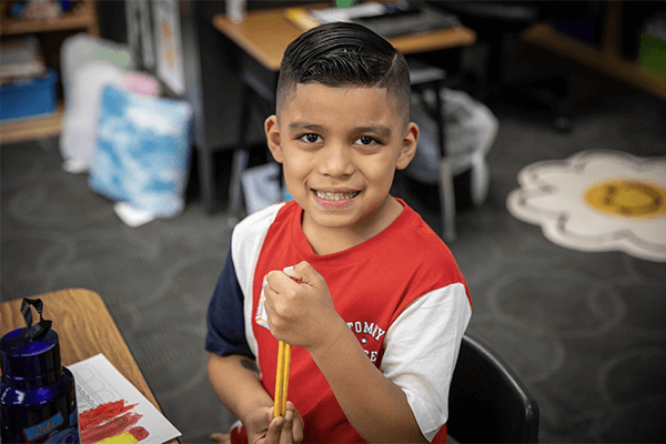 A young multilingual student at Kansas City, Kansas Public Schools sits happily working at his desk in a classroom.