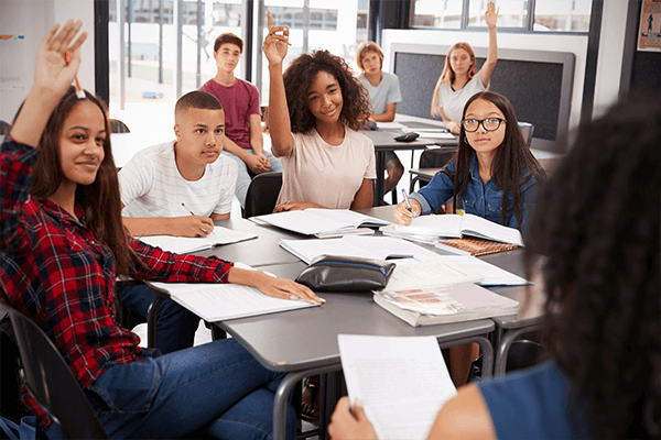 A group of middle grade students at desks engaging with a teacher.
