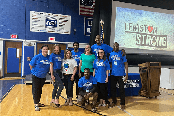 a group of Lewiston Public Schools staff members standing in a gymnasium smiling in front of a screen that reads Lewiston Strong.