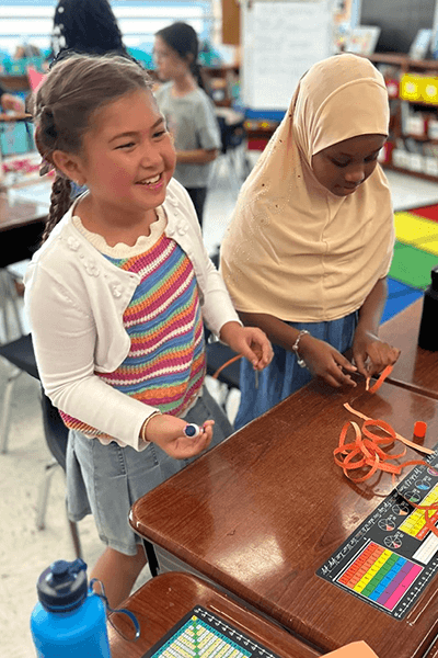 Two Lewiston Public Schools elementary-aged students laughing and engaging in their learning at school.