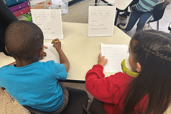 Two Lewiston Public Schools students sitting side by side at a table working on a writing lesson. 