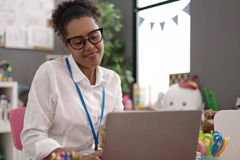 A teacher at her desk in front of her laptop writing an email to parents.