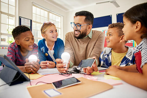 Diverse learners and a teacher in an elementary classroom participate in a hands-on science demonstration exploring how electricity and light bulbs work.