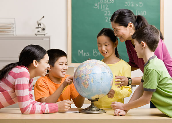 A group of young students surrounding a globe on a table with a teacher learning about geography.