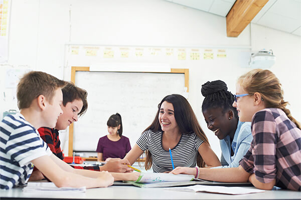 A group of high school students working together happily in a group on an inquiry-based social studies project.