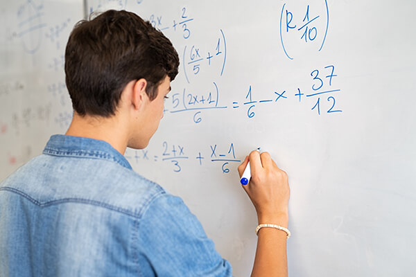 Photo of an individual high school student in a classroom working on a math problem.