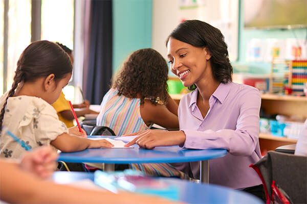 A teacher is providing one-on-one differentiated instruction to an elementary student at their desk.
