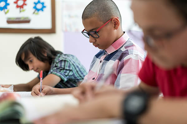 A middle school student sits at his desk working on a writing assignment.