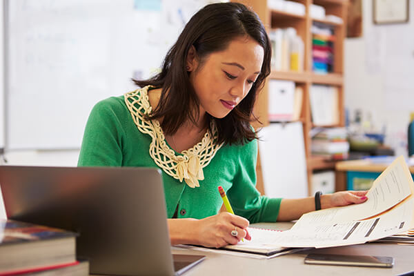 A teacher works at her desks reviewing her students’ writing assignments.